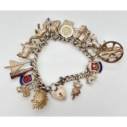 A vintage silver charm bracelet with padlock clasp and 20 assorted silver & white metal charms. Charms include rickshaw, coke bottle, Concorde, enameled shields, terrier dog, horses, dolphin and a church that opens to reveal a bride and groom. Silver marks on some charms. Bracelet padlock hallmarked Birmingham 1963. Total weight approx. 79.6g.