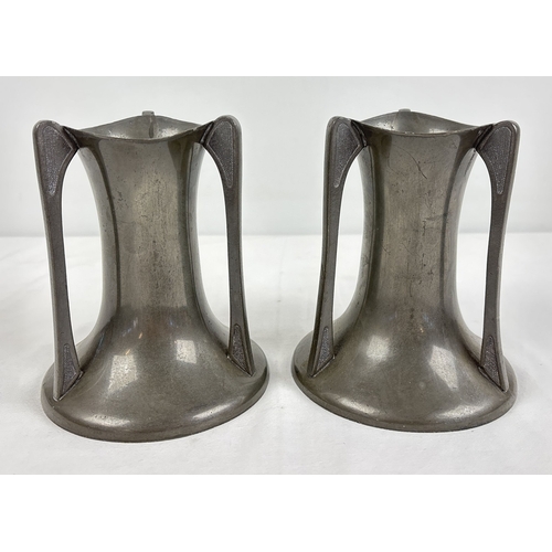 A pair of Arts & Crafts organic shaped pewter vases with soft fluted rims on a concaved body with broad bases. 3 uprights to each vase with hammered effect panel to top and bottom of each. Marked Pewter 0997 with crossed arrows to each base. Approx 15 cm tall.