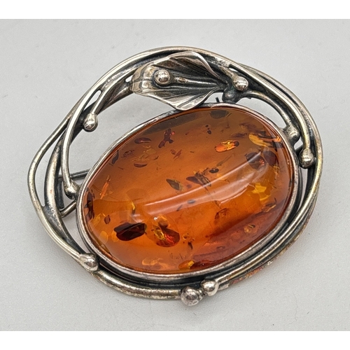 A white metal Art Nouveau style brooch/pendant set with an oval piece of cognac amber. Sinuous design to mount with Arum lily detail. Pin and hanging bale to back. Not hallmarked. Approx. 4 x 3.5cm.