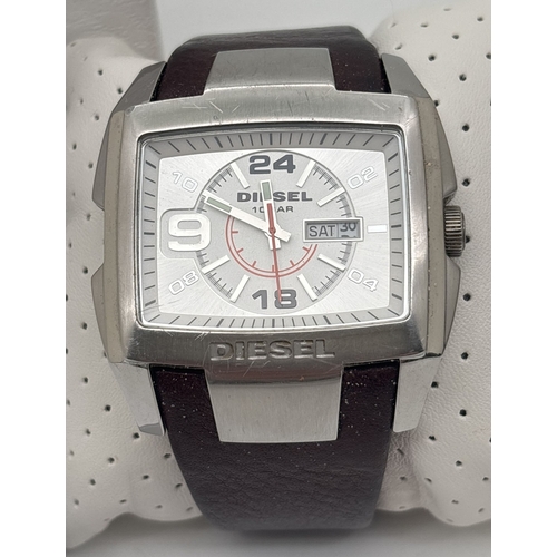 A boxed men's Only The Brave DZ 1273 wristwatch by Diesel. Stainless steel square case with brown leather strap and stainless steel buckle. Brushed silver and white face with silver and black hour markers. Luminous detail to hands, with bright orange seconds hand. Day and date window to right side of face. With instruction manual. Not working, possibly needs battery change.