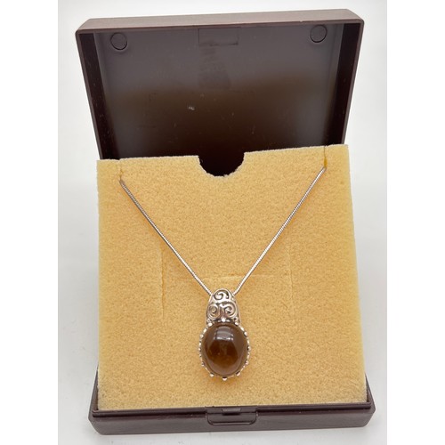 1056 - A boxed silver pendant set with an oval smoked quartz cabochon with claw mount and pierced scroll wo... 