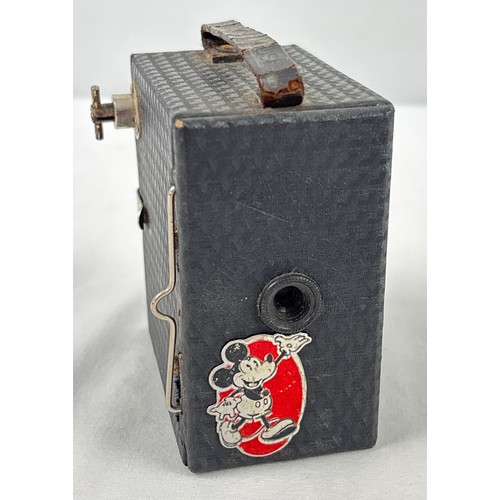 An Art Deco Ensign Mickey Mouse box camera by Houghton-Butcher, from 1935. Small 9cm tall wooden box construction covered in Art Deco Geometric pattern covering, featuring a foil decal of Mickey Mouse on front under the lens, and a faux leather named strap. Uses an M10 film.