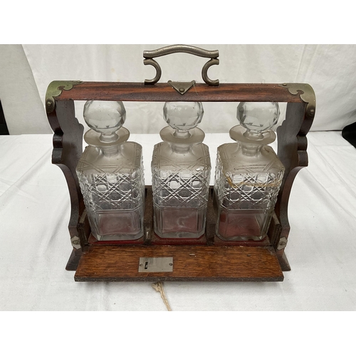 134 - ANTIQUE OAK TANTALUS WITH 3 CUT GLASS BOTTLES (1 A/F) WITH PLATED FITTINGS AND KEY H11