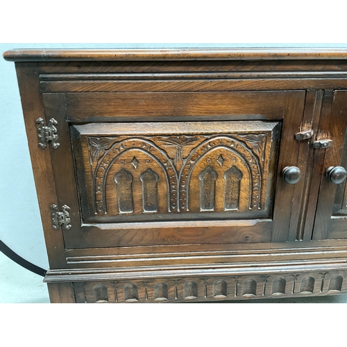 327 - DARK OAK PRIORY STYLE TWO DOOR CABINET WITH CARVED PANELS SHAPED FREEZE ON STRETCHERED BASE H33