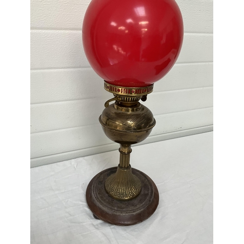 94 - BRASS OIL LAMP ON WOODEN BASE COMPLETE WITH RED GLASS SHADE - NO GLASS FUNNEL