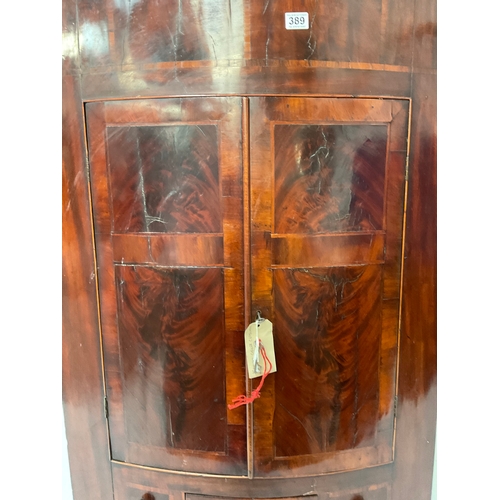 389 - GEORGIAN MAHOGANY INLAID BOW FRONTED HANGING CORNER CABINET WIHT DRAWER TO BASE FITTED WITH SHELVES ... 