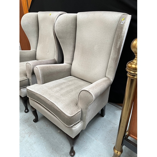 397 - TWO GREEN UPHOLSTERED WINGBACK FIRESIDE CHAIRS ON FRONT CABRIOLE FEET.