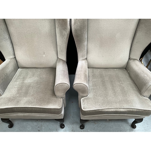 397 - TWO GREEN UPHOLSTERED WINGBACK FIRESIDE CHAIRS ON FRONT CABRIOLE FEET.