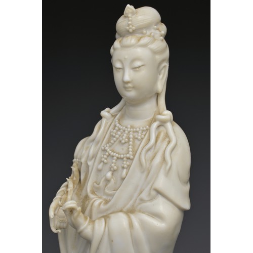 29 - A CHINESE BLANC DE CHINE FIGURE OF GUANYIN. The moulded figure of Guanyin standing on a dragon cover... 