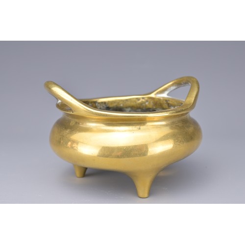 51 - A CHINESE POLISHED BRONZE TRIPOD CENSER. With two raised looped handles on three short feet. Raised ... 