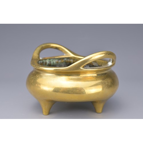 51 - A CHINESE POLISHED BRONZE TRIPOD CENSER. With two raised looped handles on three short feet. Raised ... 