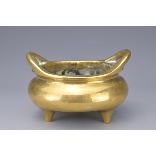 51 - A CHINESE POLISHED BRONZE TRIPOD CENSER. With two raised looped handles on three short feet. Raised ... 