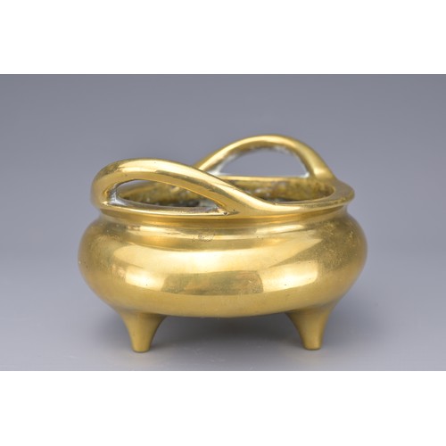 51 - A CHINESE POLISHED BRONZE TRIPOD CENSER. With two raised looped handles on three short feet. Raised ... 