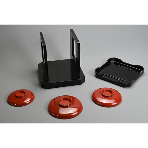 288 - A SET OF THREE 20TH CENTURY RED LACQUER JAPANESE SAKE CUPS (SAKAZUKI) AND A BLACK LACQUER TABLE (KAG... 