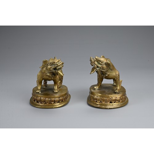 85 - A MIRRORED PAIR OF TIBETAN BRONZE TEMPLE LIONS, 19/20TH CENTURY. Each standing with their tongues ou... 