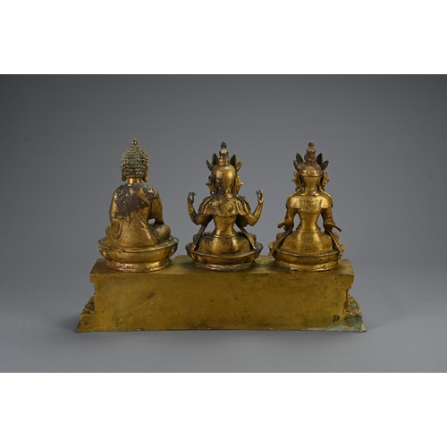 188 - A TRIO OF TIBETAN BRONZE SEATED BUDDHAS ON STAND. The deities dressed in robes adorned with jewels o... 