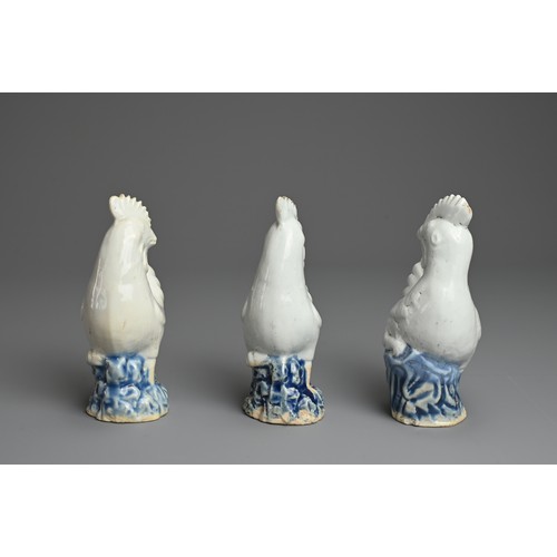 6 - THREE CHINESE BLUE AND WHITE PORCELAIN MODELS OF ROOSTERS, QING DYNASTY. Each standing on a rockwork... 