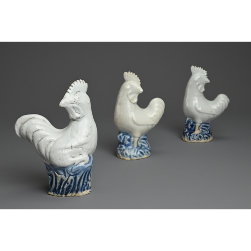 6 - THREE CHINESE BLUE AND WHITE PORCELAIN MODELS OF ROOSTERS, QING DYNASTY. Each standing on a rockwork... 