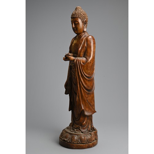 255 - A CHINESE CARVED WOODEN FIGURE OF BUDDHA, 20TH CENTURY. Standing on a lotus base dressed in robes ho... 