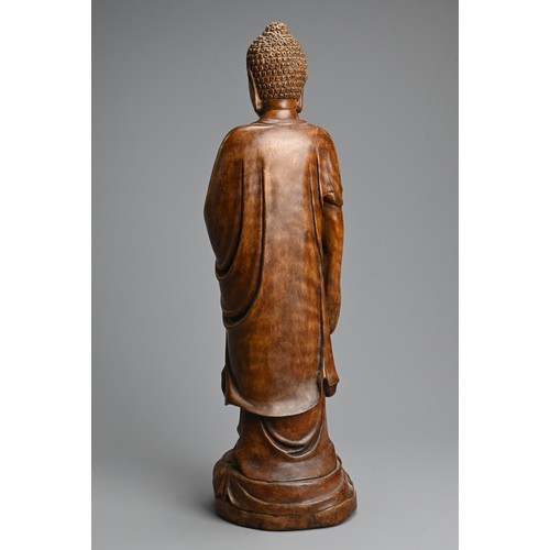 255 - A CHINESE CARVED WOODEN FIGURE OF BUDDHA, 20TH CENTURY. Standing on a lotus base dressed in robes ho... 