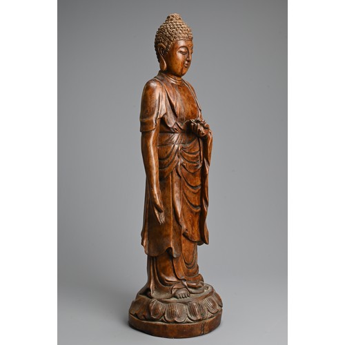 255 - A CHINESE CARVED WOODEN FIGURE OF BUDDHA, 20TH CENTURY. Standing on a lotus base dressed in robes ho... 