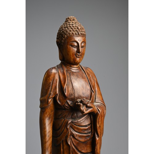 255 - A CHINESE CARVED WOODEN FIGURE OF BUDDHA, 20TH CENTURY. Standing on a lotus base dressed in robes ho... 