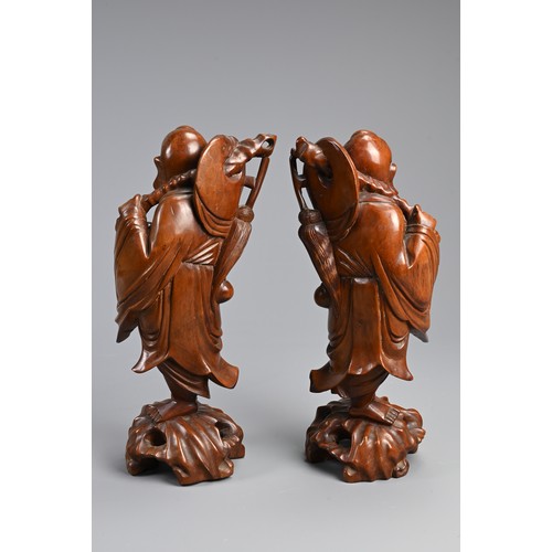 198 - A PAIR OF CHINESE CARVED WOODEN FIGURES, EARLY 20TH CENTURY. A mirrored pair each holding a bat and ... 