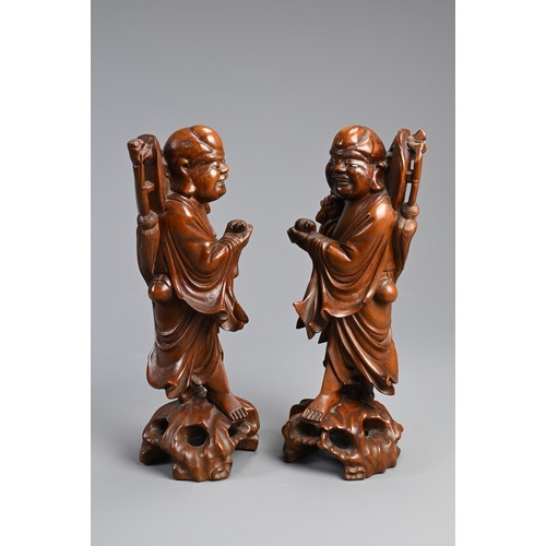 198 - A PAIR OF CHINESE CARVED WOODEN FIGURES, EARLY 20TH CENTURY. A mirrored pair each holding a bat and ... 