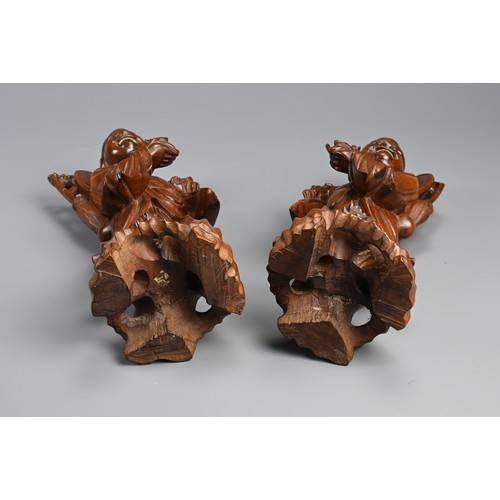 198 - A PAIR OF CHINESE CARVED WOODEN FIGURES, EARLY 20TH CENTURY. A mirrored pair each holding a bat and ... 