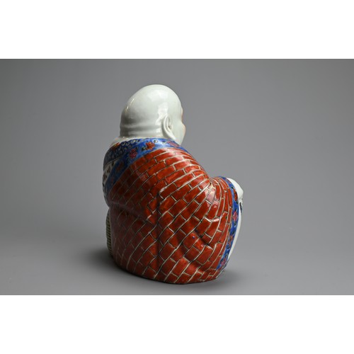 71 - A CHINESE FAMILLE ROSE PORCELAIN FIGURE OF BUDAI, 20TH CENTURY. The laughing Buddha seated dressed i... 