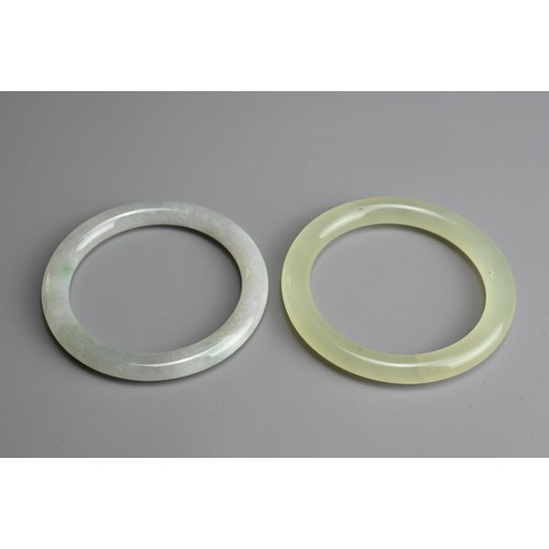 81 - TWO JADE BANGLES. Of pale green and greyish tones. Internal diameters 5.8cm and 6cm. (2)