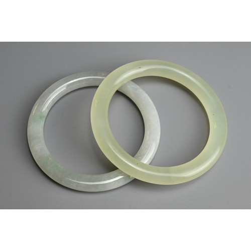 81 - TWO JADE BANGLES. Of pale green and greyish tones. Internal diameters 5.8cm and 6cm. (2)