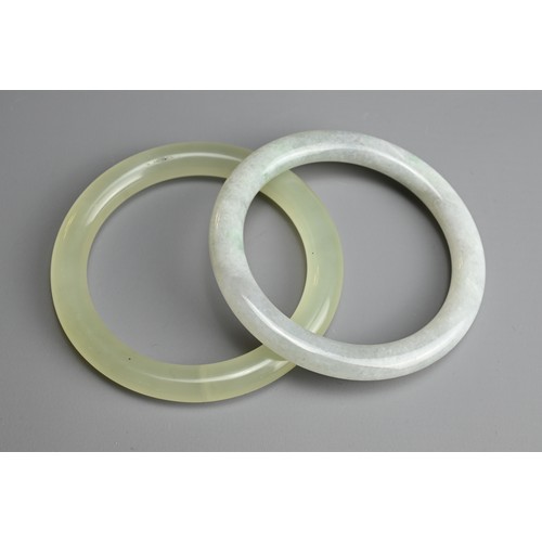 81 - TWO JADE BANGLES. Of pale green and greyish tones. Internal diameters 5.8cm and 6cm. (2)