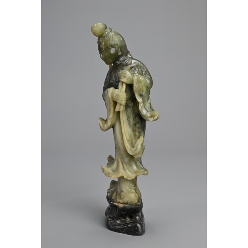 36 - A CHINESE SOAPSTONE CARVING OF GUANYIN, 20TH CENTURY. Standing dressed in robes holding lotus stems.... 