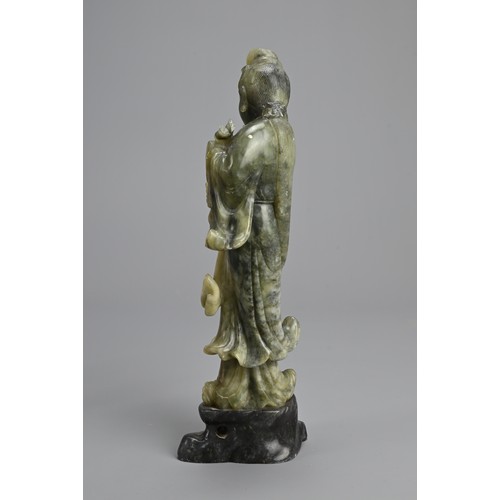 36 - A CHINESE SOAPSTONE CARVING OF GUANYIN, 20TH CENTURY. Standing dressed in robes holding lotus stems.... 