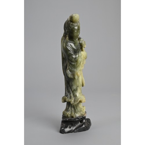 36 - A CHINESE SOAPSTONE CARVING OF GUANYIN, 20TH CENTURY. Standing dressed in robes holding lotus stems.... 