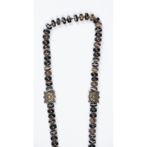 113 - A TIBETAN AGATE BEADED NECKLACE. Composed of dark circular beads with metal spacers, with tassels an... 