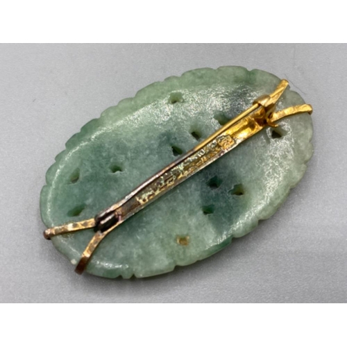 141 - 22ct yellow gold jade stone oval shaped brooch, with engraved carving