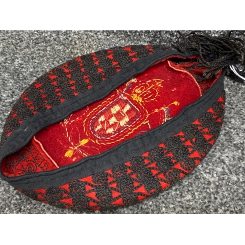 120 - Old smoking hat in red & black with needlework crest & flags to the top