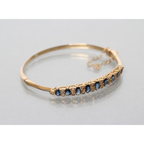 165 - A SAPPHIRE AND DIAMOND STIFF HINGED BANGLE, the upper section grain set with nine oval facet cut sap... 