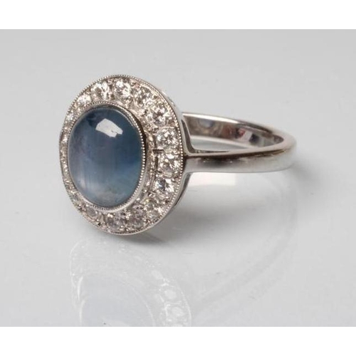 186 - A SAPPHIRE AND DIAMOND DRESS RING, the oval cabochon polished sapphire open back collet set to a bor... 