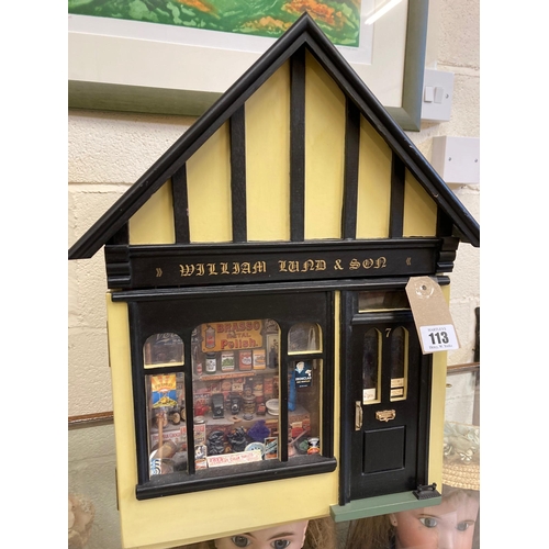 113 - A doll's house village shop, of painted wood construction, with well filled display window, external... 