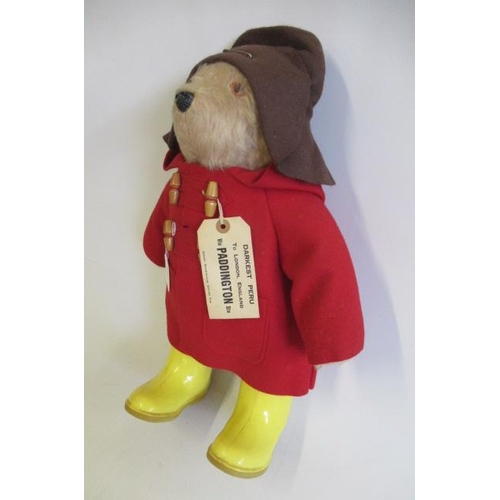 141 - A Paddington bear, with amber eyes, plastic nose, felt red coat, yellow Dunlop boots, Brown hat and ... 