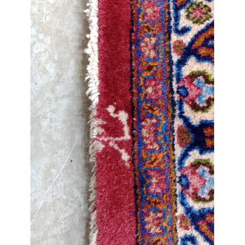 492 - A PERSIAN CARPET, the claret field with floral sprays with navy and tangerine central gul and matchi... 