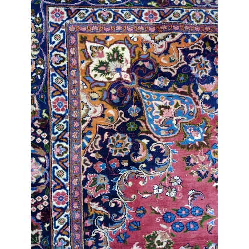 492 - A PERSIAN CARPET, the claret field with floral sprays with navy and tangerine central gul and matchi... 