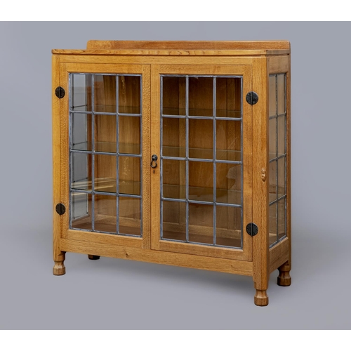 593 - A ROBERT THOMPSON ADZED OAK DISPLAY CABINET of canted oblong form with leaded glazed doors and sides... 