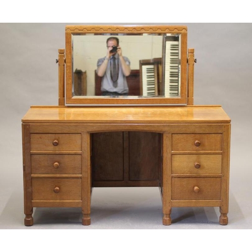 595 - A ROBERT THOMPSON ADZED OAK DRESSING TABLE, the bevelled oblong swing mirror on turned faceted suppo... 