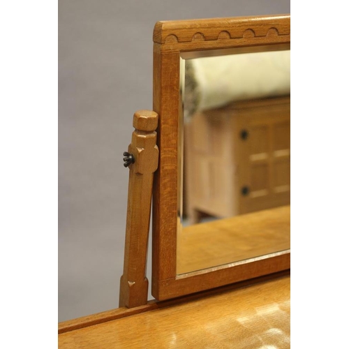 595 - A ROBERT THOMPSON ADZED OAK DRESSING TABLE, the bevelled oblong swing mirror on turned faceted suppo... 