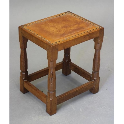 596 - A ROBERT THOMPSON ADZED OAK STOOL of oblong form with padded cow hide seat, on faceted turned and bl... 