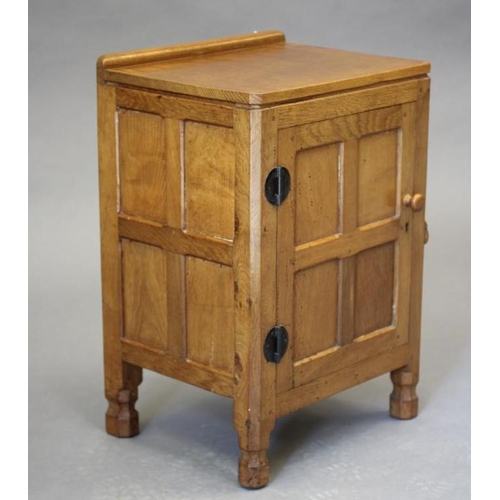 602 - A ROBERT THOMPSON ADZED OAK BEDSIDE CABINET of canted multi-panelled oblong form, the moulded edged ... 